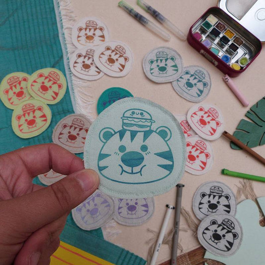 Broche dessinée, sérigraphiée et cousue à la main. Tigre mignon avec un burger sur la tête. Collaboration avec l'artiste Yetitia.