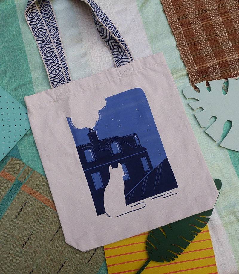 Grand totebag fabriqué en matières recyclées et imprimé en France représentant un paysage nocturne paisible. Ambiance calme d'une ville de nuit, avec un chat qui regarde les toits.