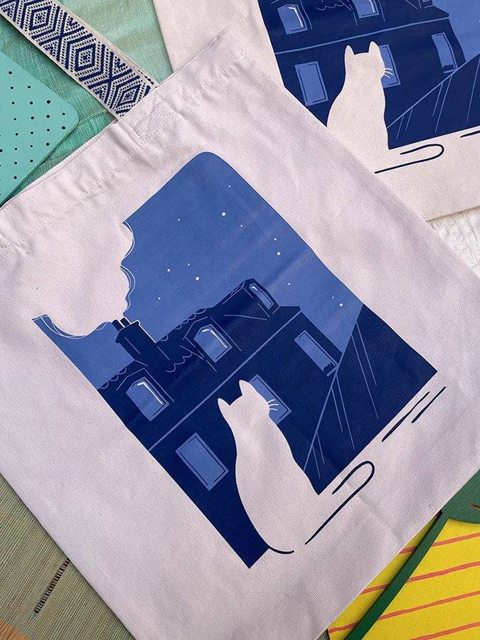 Grand totebag fabriqué en matières recyclées et imprimé en France représentant un paysage nocturne paisible. Ambiance calme d'une ville de nuit, avec un chat qui regarde les toits.