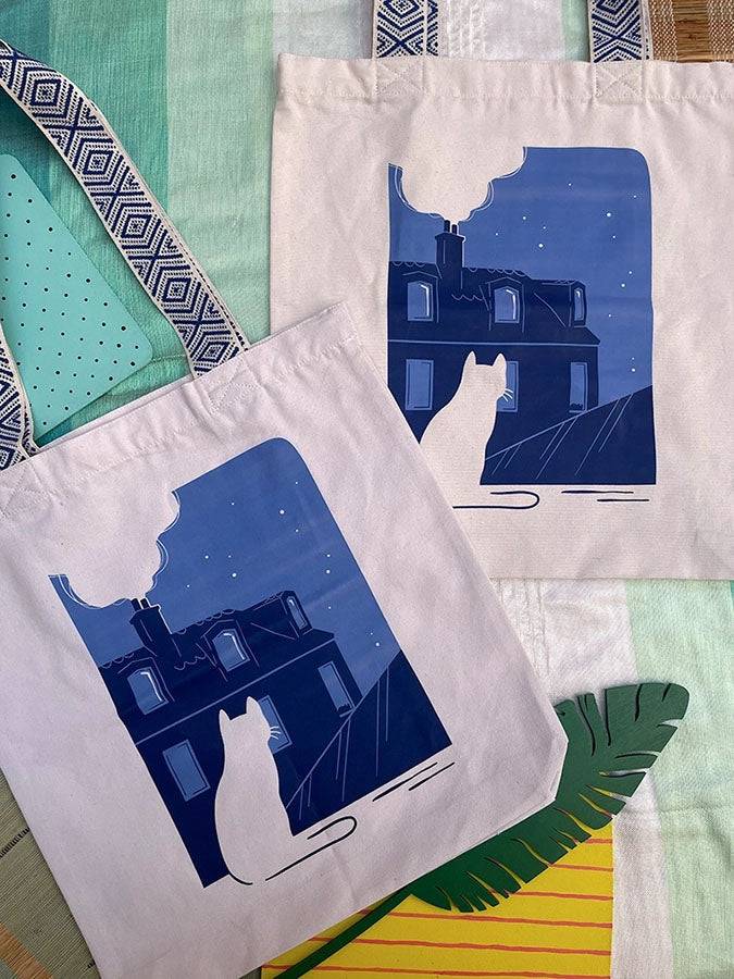 Grand totebag fabriqué en matières recyclées et imprimé en France représentant un paysage nocturne paisible. Ambiance calme d'une ville de nuit, avec un chat qui regarde les toits.