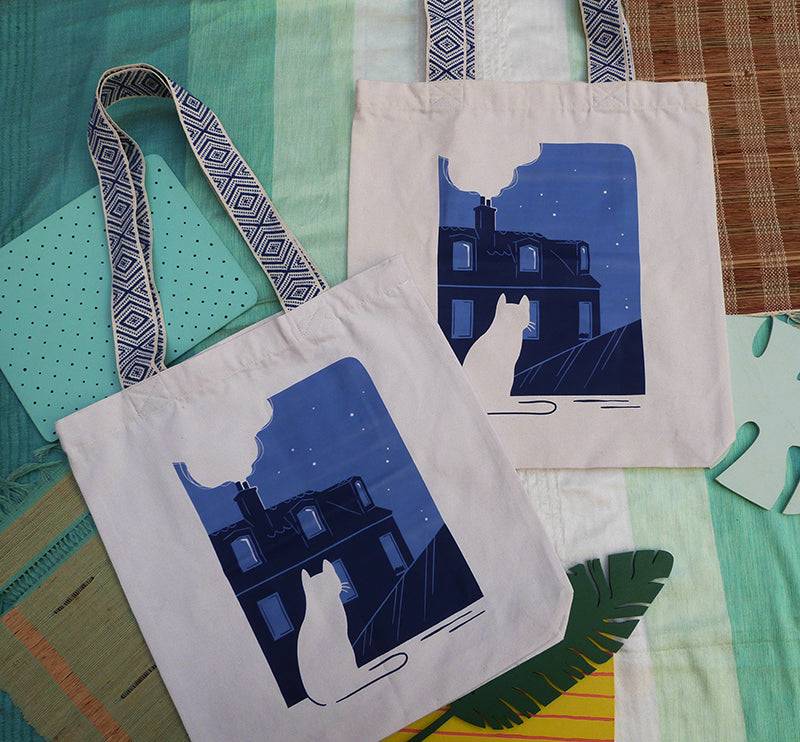 Grand totebag fabriqué en matières recyclées et imprimé en France représentant un paysage nocturne paisible. Ambiance calme d'une ville de nuit, avec un chat qui regarde les toits.