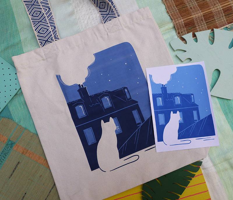 Grand totebag fabriqué en matières recyclées et imprimé en France représentant un paysage nocturne paisible. Ambiance calme d'une ville de nuit, avec un chat qui regarde les toits.